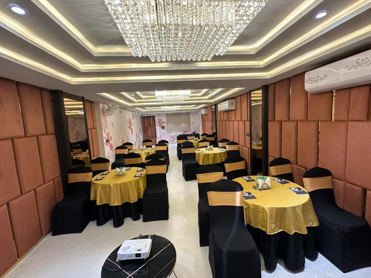 A banquet hall with round tables, black and gold chairs, and a chandelier.