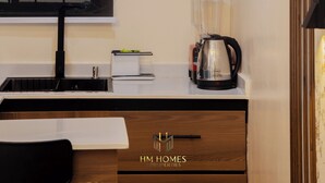 Une cuisine moderne dotée d’une fenêtre à cadre noir, d’un plan de travail blanc, d’une machine à café et d’un luminaire fixé au mur.