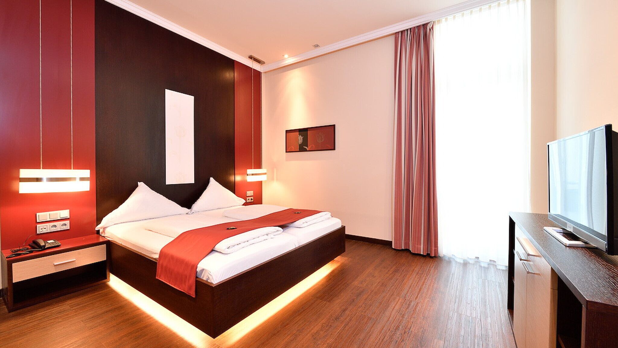 Una camera d'albergo moderna con un letto grande, comodini, una TV e un quadro appeso al muro.