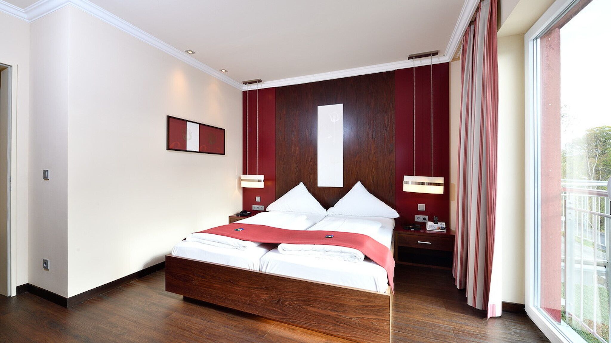 A modern hotel room with a large bed, wooden headboard, and a view through a large window.