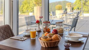 A breakfast table with a basket of pastries, a glass of orange juice, and a vase with flowers. - Dormio Hotel der Seehof (Heimbach)