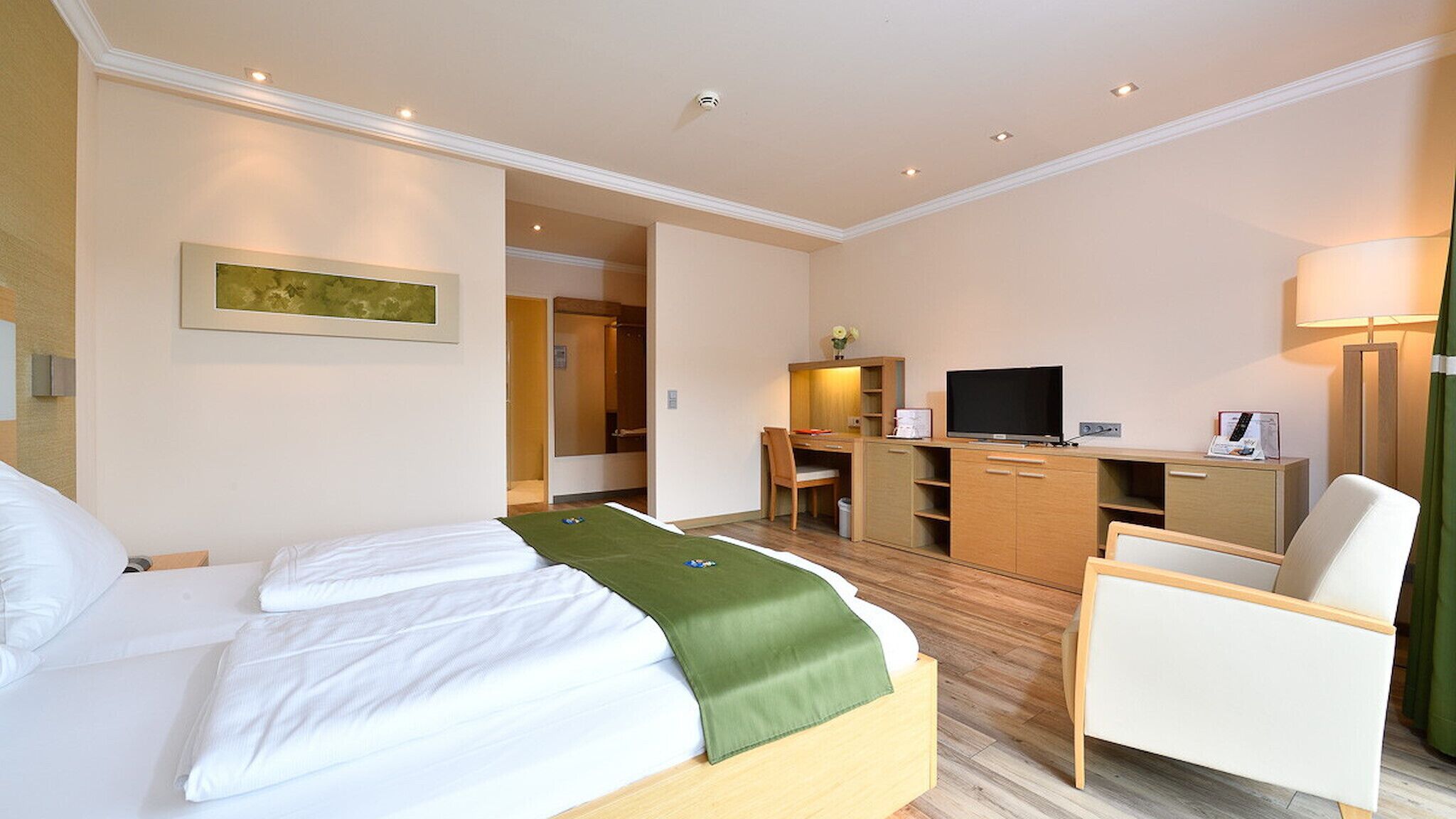 A hotel room with a bed, a desk, a chair, a television, and a lamp.