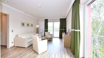 Una sala de estar moderna con un sofá, sillones, una mesa de centro y un balcón con cortinas verdes.