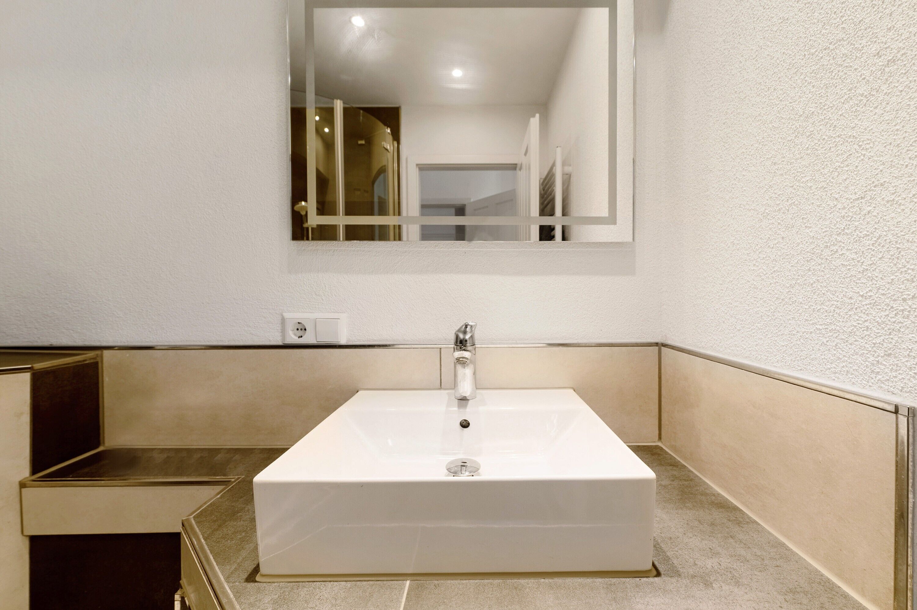 A bathroom with a white sink, a mirror, and a door leading to another room.