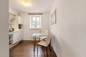 A compact kitchen with white cabinets, a glass table, and a window with a view.