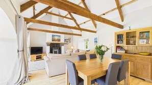Un'ampia zona giorno con un tavolo da pranzo in legno, sedie rivestite di grigio, un divano e un angolo cottura con mobili in legno e una TV.