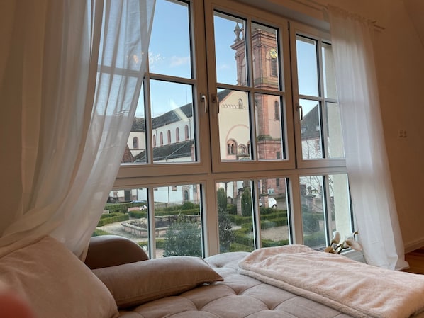 Une chambre avec une grande fenêtre, un lit et une vue sur un bâtiment doté d’une tour horloge.