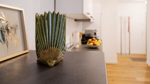 Eine Küche mit einem gerahmten Kunstwerk, einem grünen Strauß und einer Obstschale im Hintergrund.