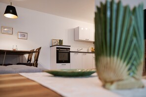 Una cocina moderna con armarios blancos, horno empotrado y comedor con mesa y sillas.