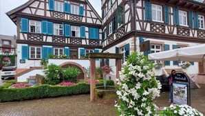 Ein traditionelles Fachwerkhäuschen mit Balkon, Schild und Blumenarrangement.