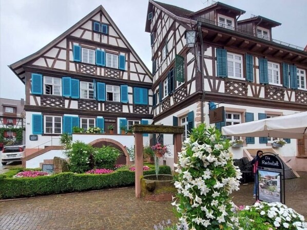 Un edificio tradicional con entramado de madera, un balcón, un letrero y un arreglo floral.