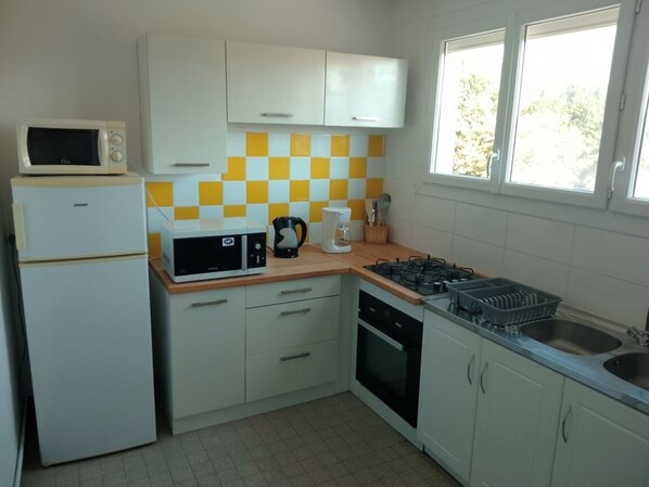 A compact kitchen with white cabinets, a microwave, a stove, and a sink.