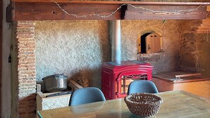 A rustic interior with exposed wooden beams, a stone wall, a red wood-burning stove, and a table with chairs. - Gîte in the heart of the Gers - 2 hectares of tranquility 7 minutes from the Circuit de Nogaro (Magnan)