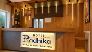 A hotel reception desk with a sign indicating A/C, Non A/C, and Deluxe Rooms. - Hotel Radhika (Somnath)