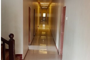 A long, narrow hallway with a polished floor and wooden doors on either side. - Hotel Radhika (Somnath)