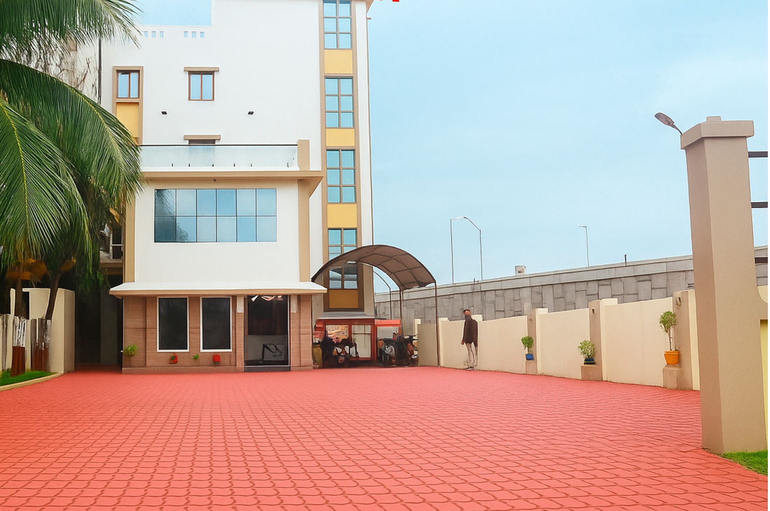 A modern building with a red brick entrance, a covered waiting area, and a person standing near the entrance.