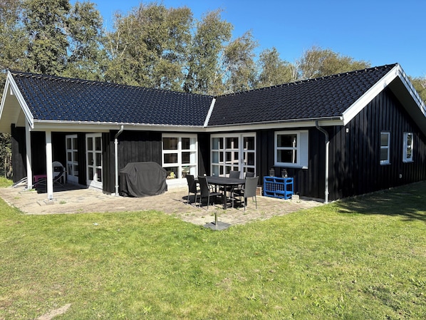 A house with a covered patio, a table with chairs, and a blue storage bin.