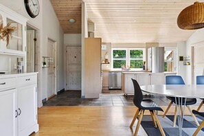 Moderni keittiö, jossa on valkoiset kaapit, ruokapöytä tuoleineen ja suuri ikkuna.