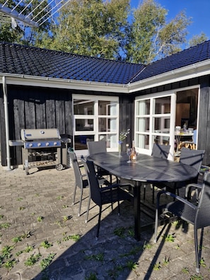 An outdoor patio with a round table and chairs, a barbecue grill, and a wooden fence.