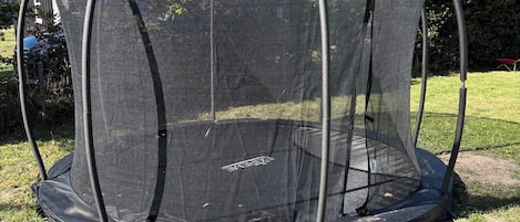 Un trampoline doté d’un filet de protection, installé dans une cour gazonnée.