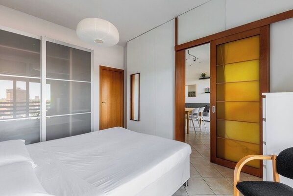 A modern hotel room with a large bed, a sliding glass door leading to a balcony, and a view of the cityscape.