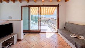 A living room with a television, a sofa, and a sliding glass door leading to a balcony. - Eden House - Terrace & View Lake (Gardone Riviera)