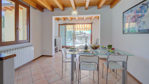 A dining area with a glass table, four chairs, and a view of the outside through large windows.