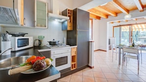 A modern kitchen with a stove, microwave, and sink. There is a dining area with a table and chairs. - Eden House - Terrace & View Lake (Gardone Riviera)