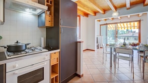 A kitchen with a stove, oven, and a refrigerator. There is a dining area with a table and chairs. - Eden House - Terrace & View Lake (Gardone Riviera)