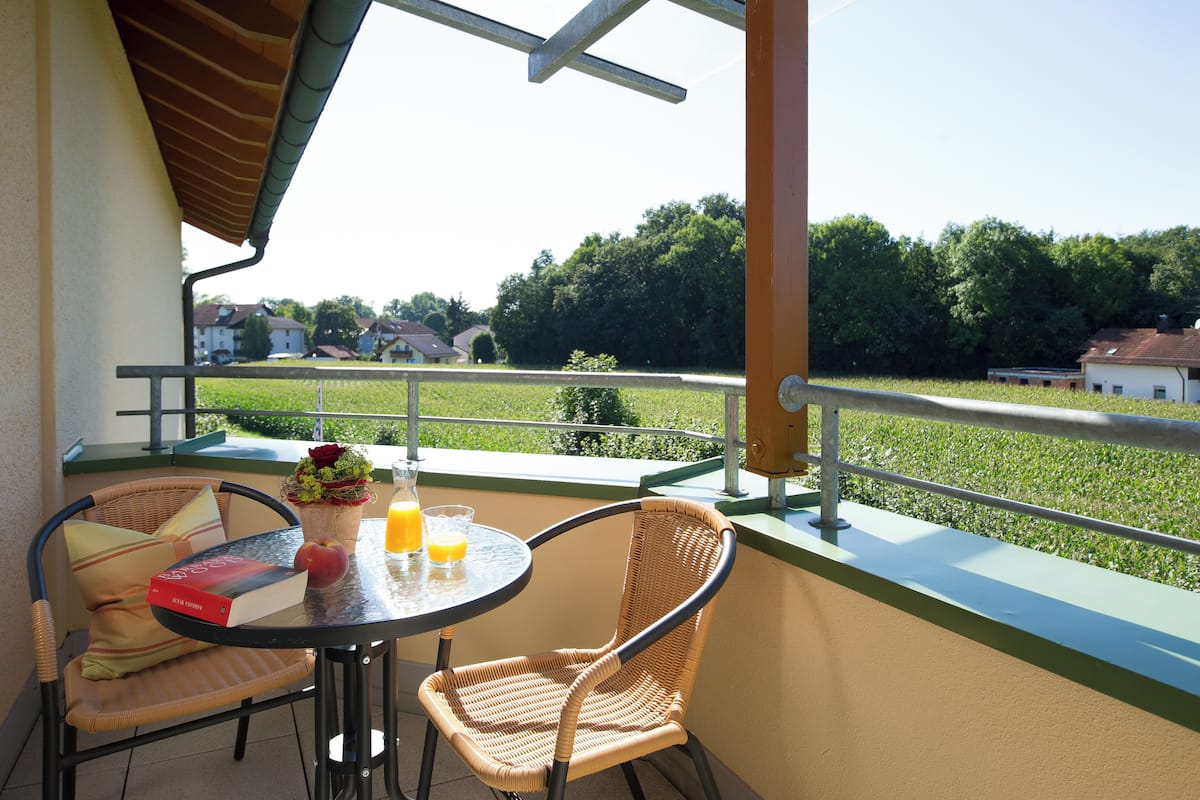 A balcony with wicker chairs, a table with a book, a glass of orange juice, and a potted plant.