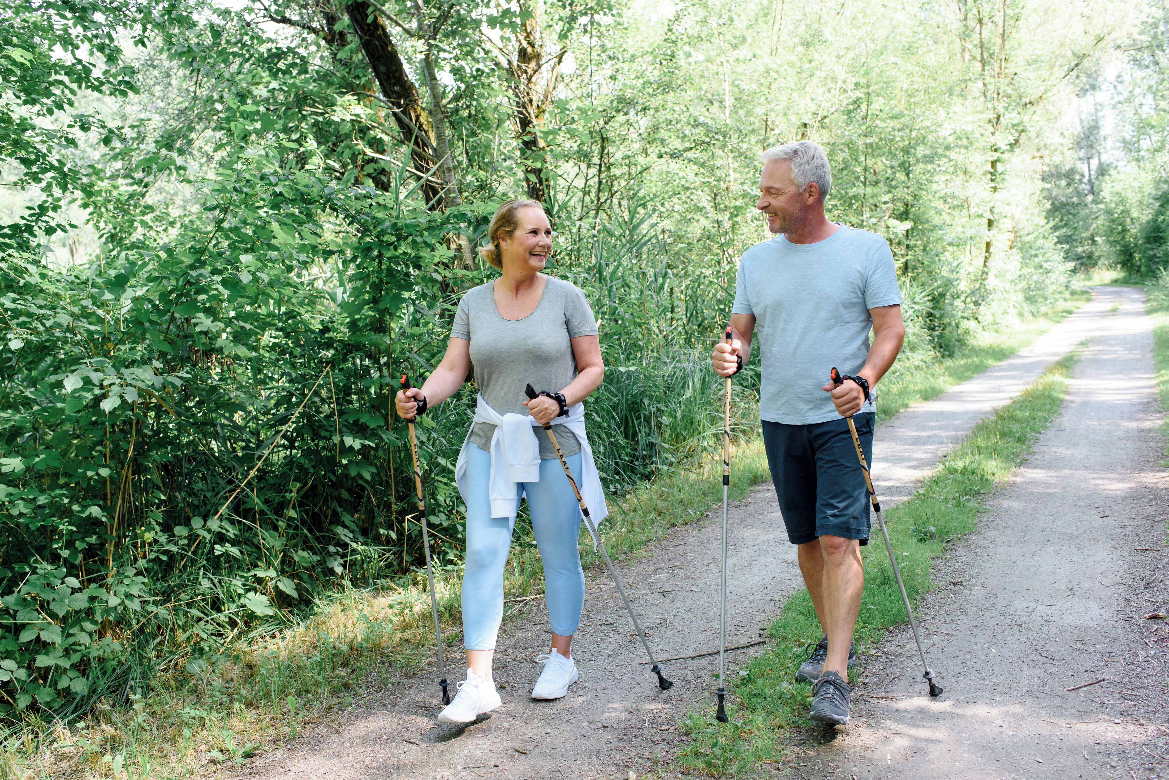 Two people walking on a dirt path surrounded by greenery.