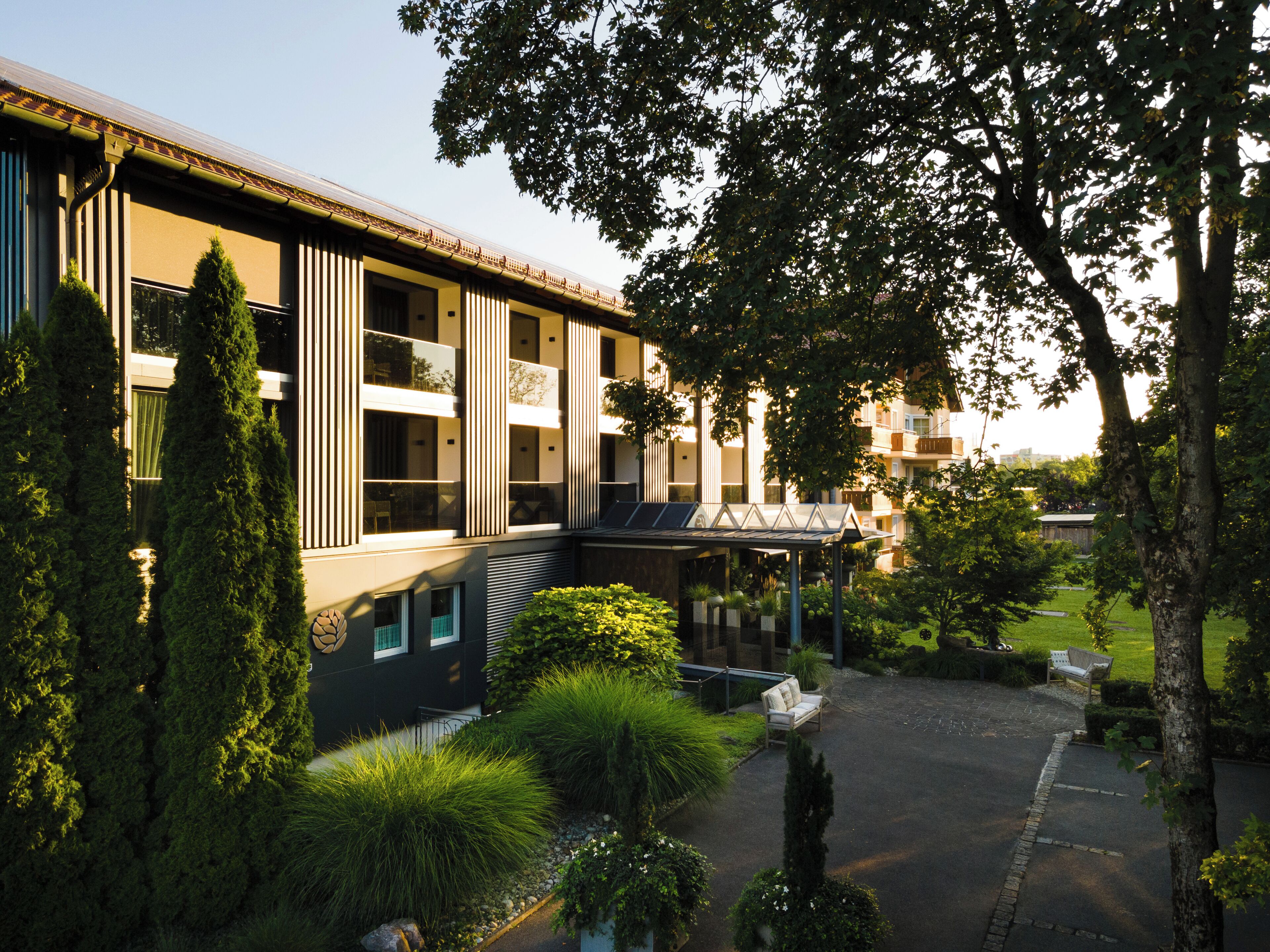 A modern building with a covered outdoor seating area, surrounded by greenery and trees.