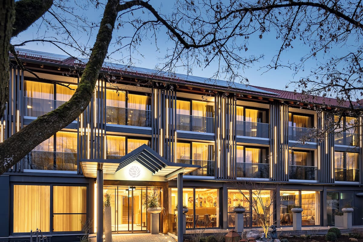 A modern hotel with a glass facade, outdoor seating, and a well-lit entrance.