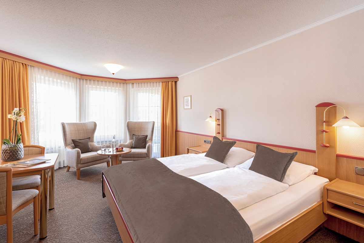 A hotel room with a large bed, two armchairs, a small table, a desk, and a lamp.