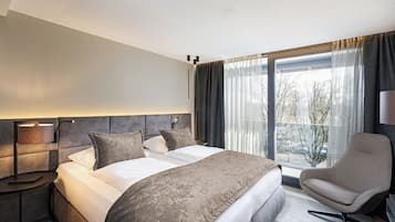A modern hotel room with a large bed, a chair, a nightstand, and a window with curtains.