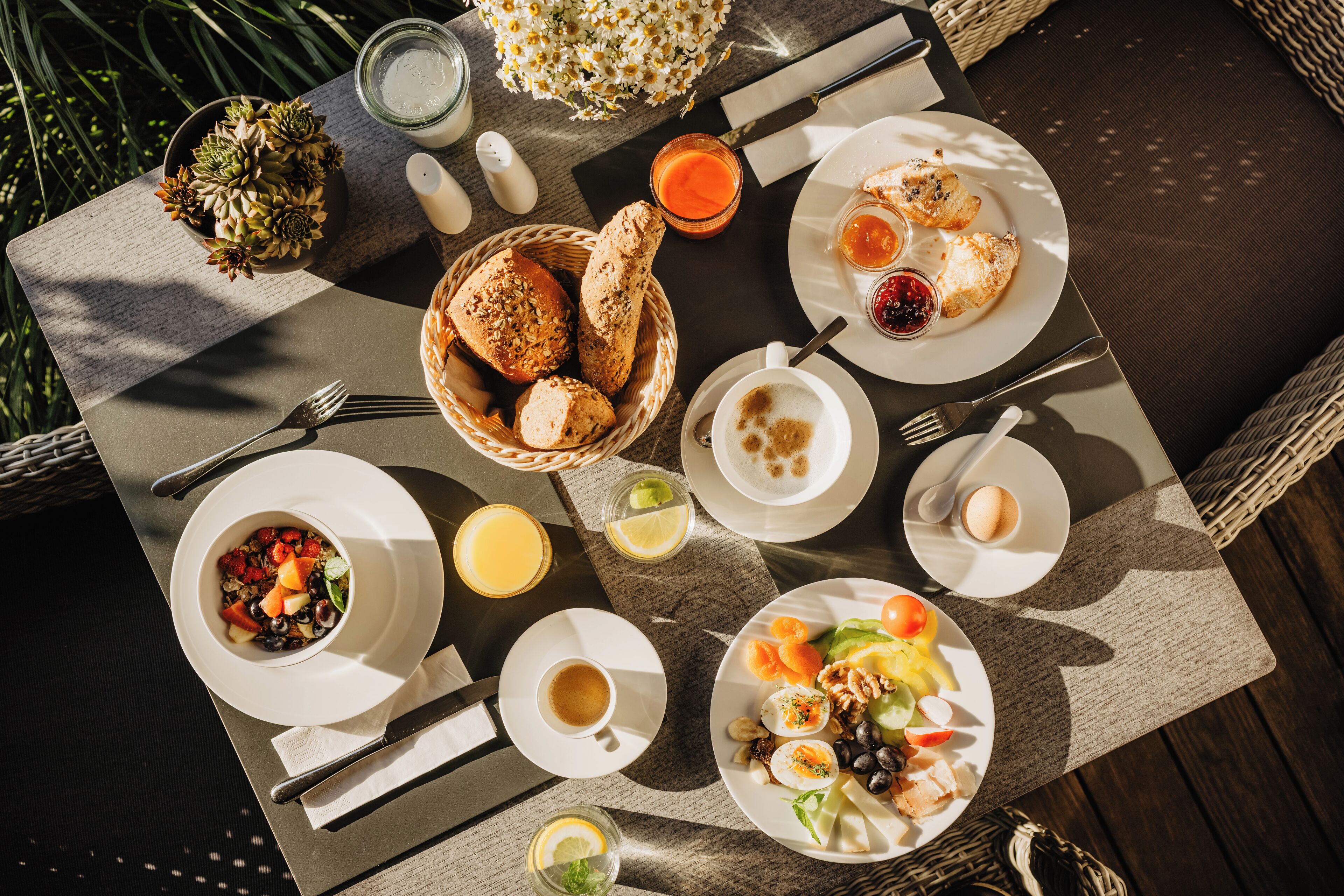 A breakfast table with various dishes, including bread, eggs, and fruit, along with cups and a bowl of soup.