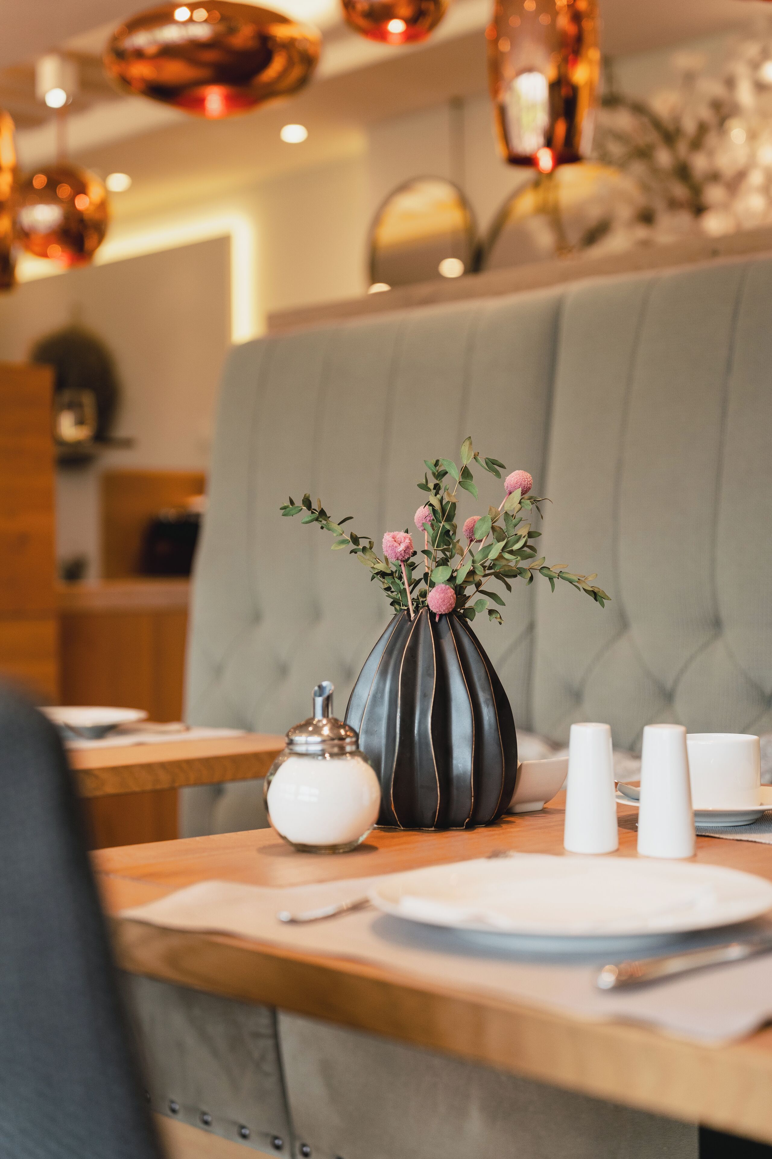 A dining table with a vase of flowers, salt and pepper shakers, and a white sugar bowl.
