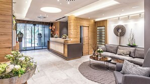 Un espace d’accueil moderne avec un comptoir de réception en bois, un canapé gris et une table basse ronde.