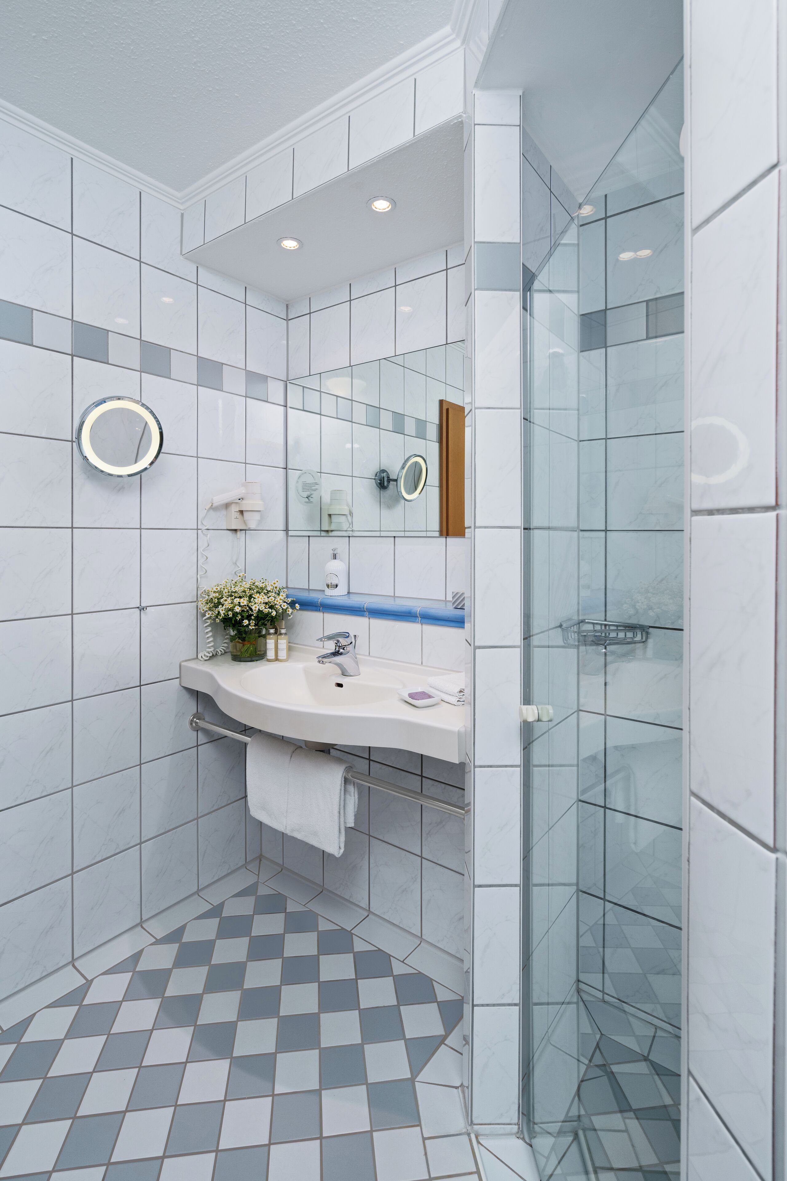 A modern bathroom with a glass shower enclosure, a white sink with a mirror, and a patterned floor.