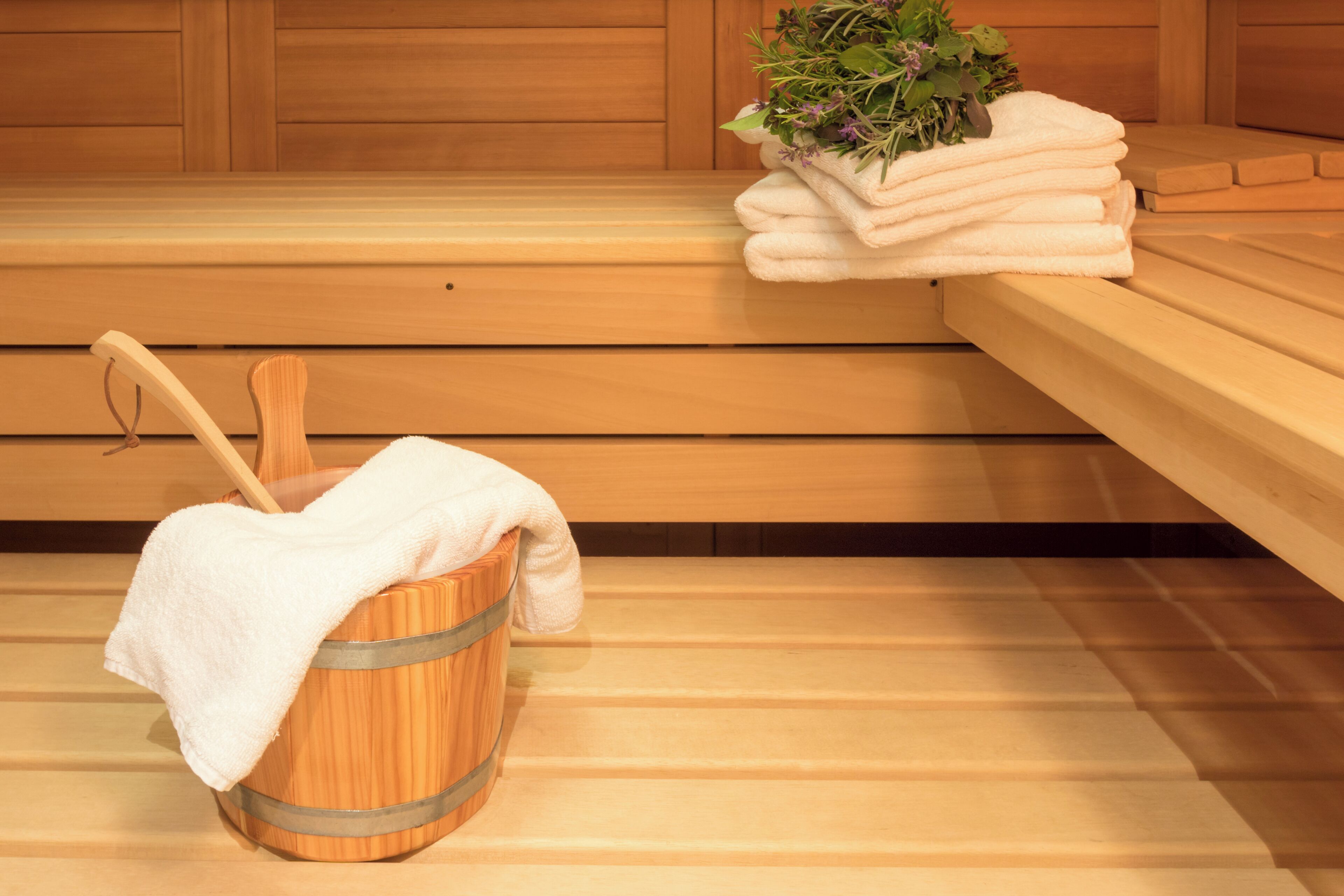 Un sauna avec des bancs en bois, un seau en bois contenant une serviette et une plante.