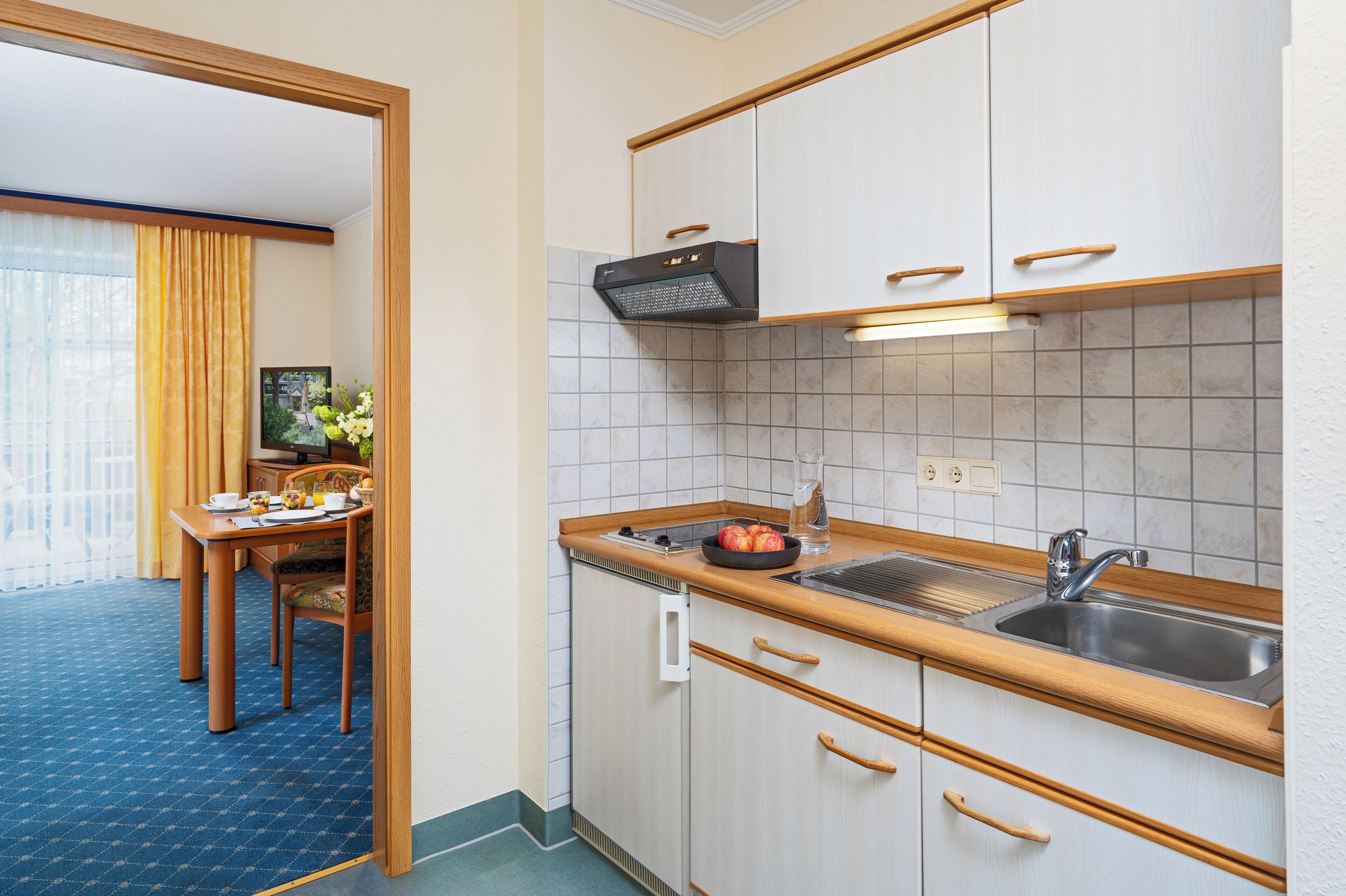 Une cuisine compacte équipée d’un évier, d’une cuisinière et de placards. Une table à manger avec des chaises se trouve dans la pièce adjacente.