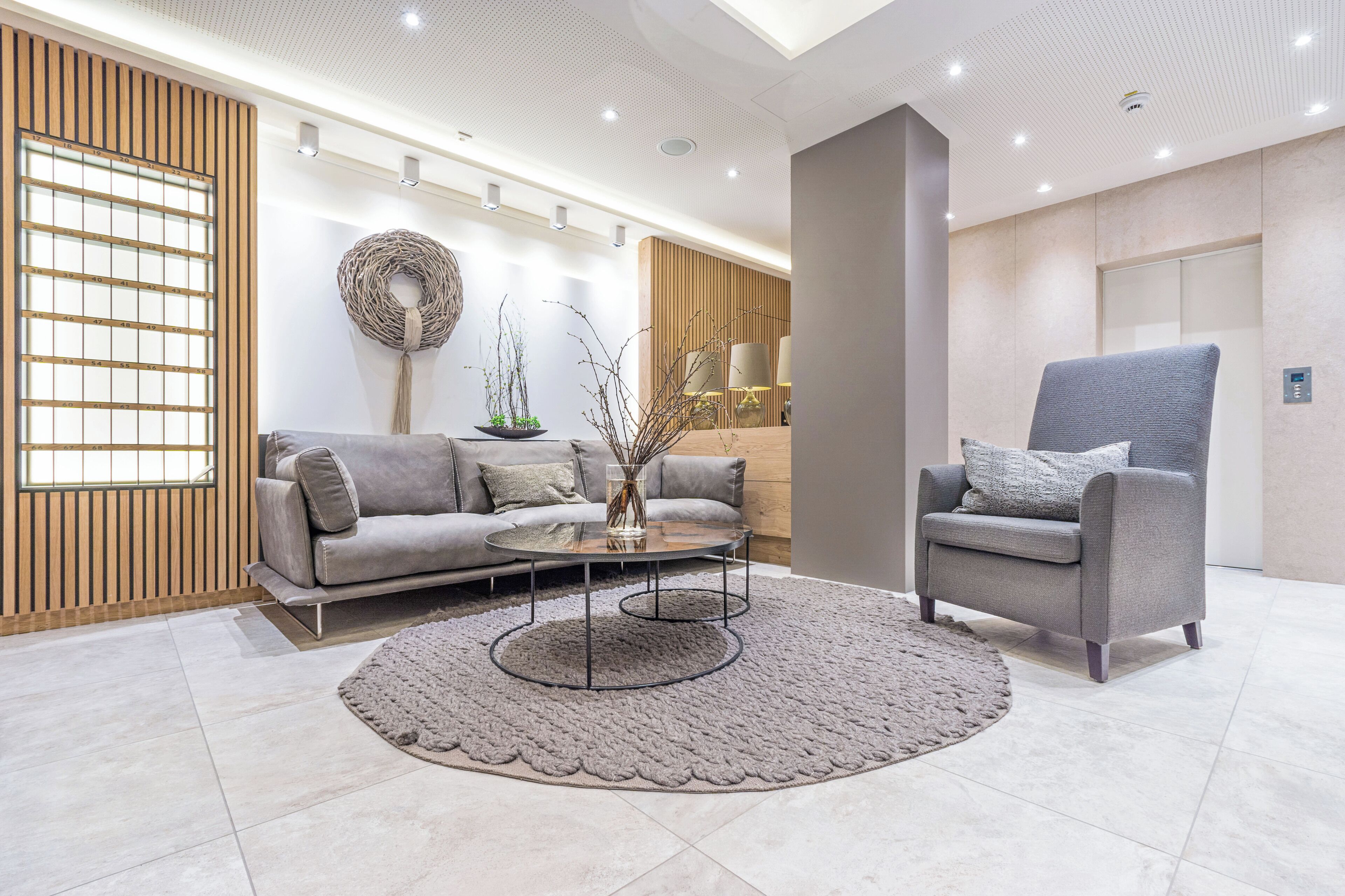 A modern living room with a grey sofa, a grey armchair, a round coffee table, and a decorative rug.