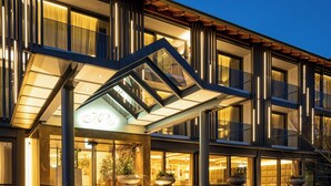 Une entrée d’hôtel moderne avec un auvent en verre, un revêtement de sol en pierre et des plantes en pot.