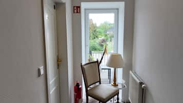 Ein schmaler Flur mit Stuhl und Lampe in der Nähe eines Fensters, einem Feuerlöscher und einer Heizung.