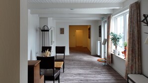 Ein Korridor mit Holzboden, ein Essbereich mit Tisch und Stühlen sowie ein Fenster mit Vorhängen.