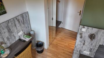Una stanza compatta con pavimento in legno, una sedia in vimini, un piccolo tavolo con un telecomando e un cestino.