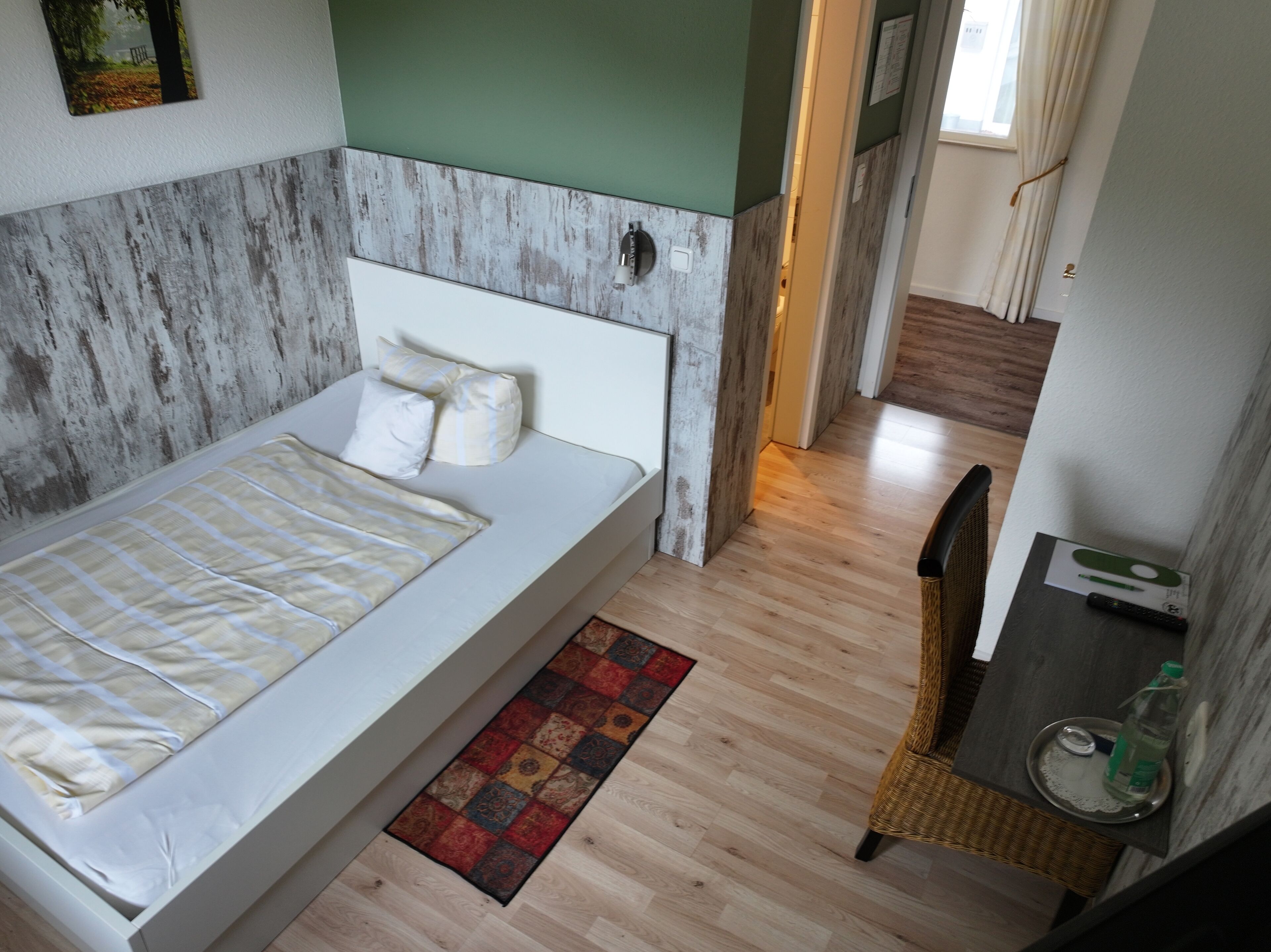 Ein Einzelbett mit weißem Kopfteil und Kissen, Holzboden, ein kleiner Teppich und ein Sessel mit Tablett.