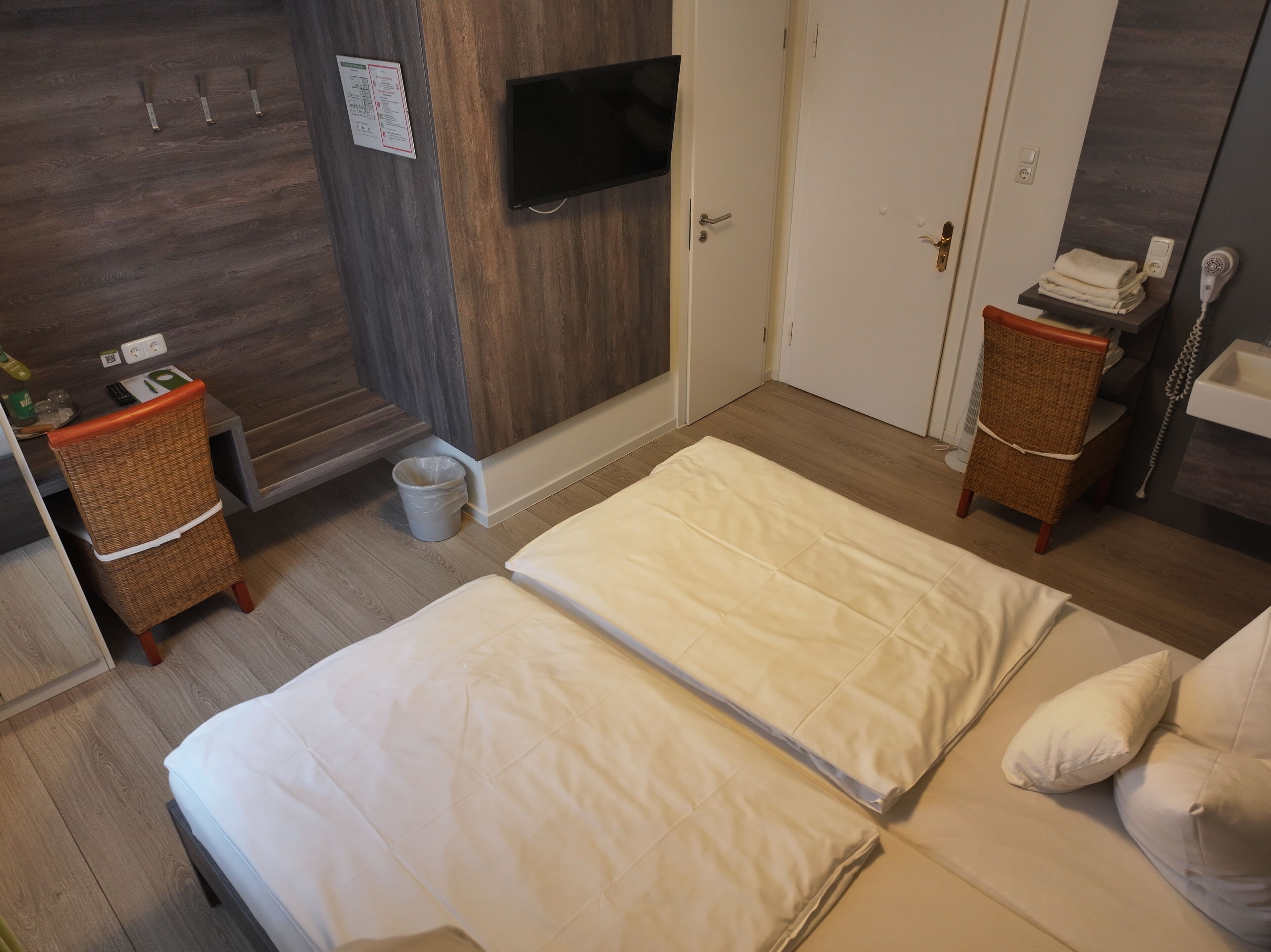 Habitació d'hotel amb llit, televisió penjada a la paret, taula petita amb cadira, bany amb rentaplatets i assecador de cabells, i terra de fusta.