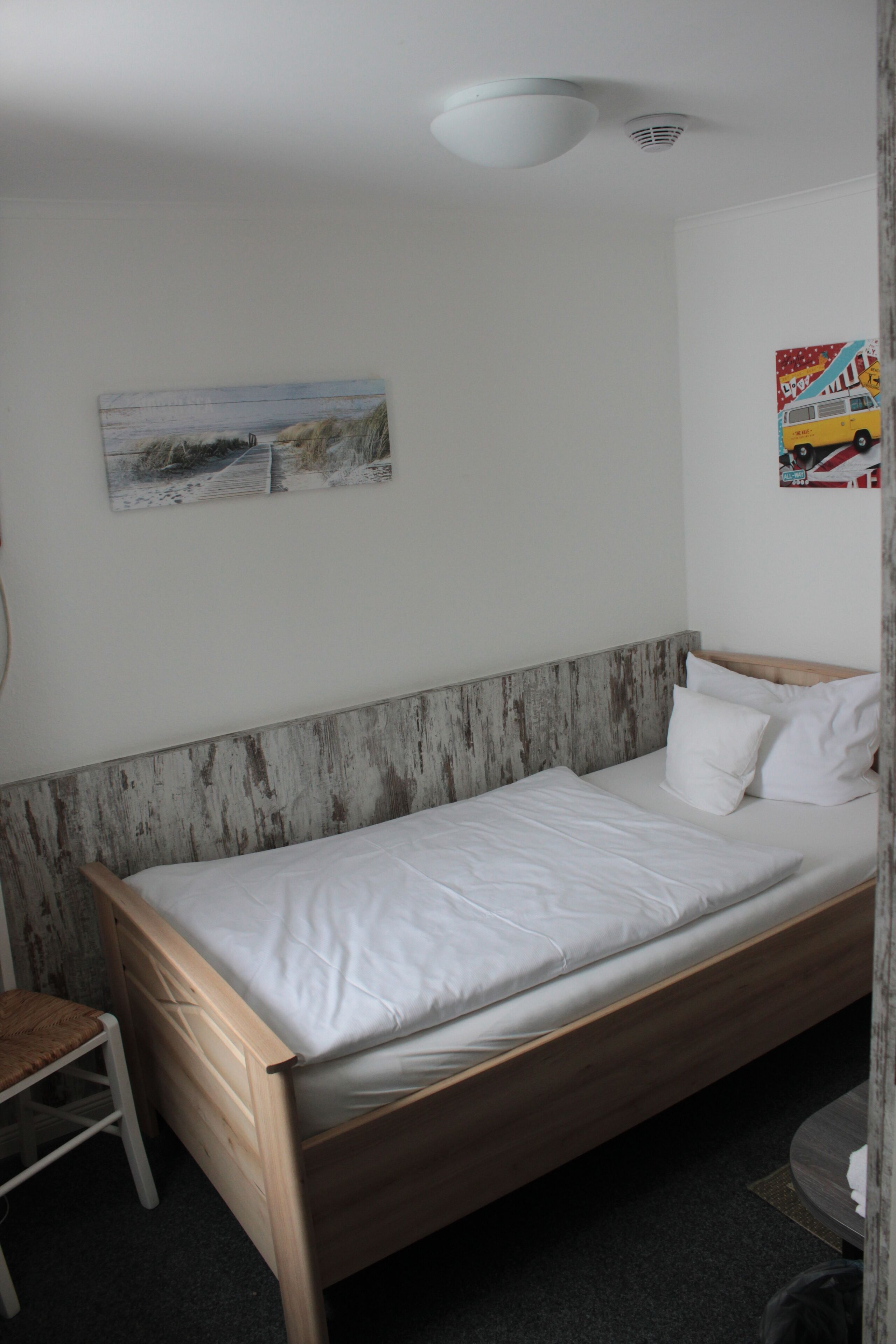 A single bed with a wooden headboard, a small bedside table, and a chair.