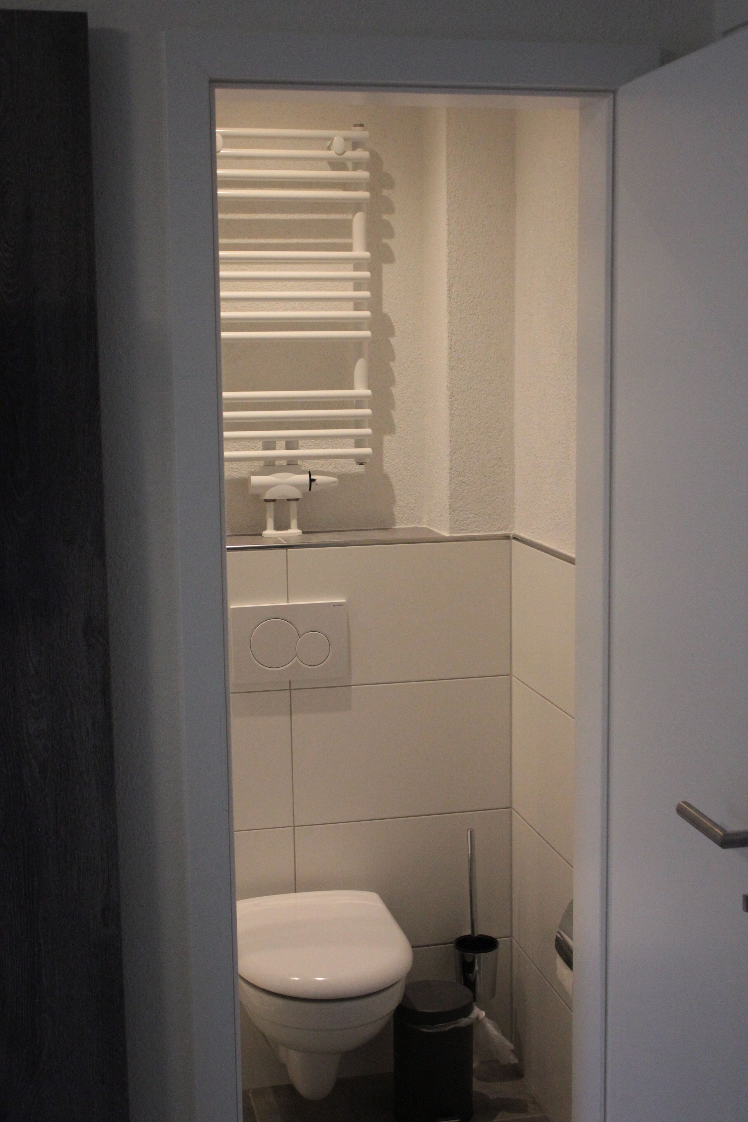 Un baño pequeño y estrecho con inodoro, un cubo de basura y un perchero para toallas.